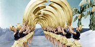 Synchron tanzende Frauen in gelben Röcken und 40er Jahre Look halten überproportionale Bananen in die Luft