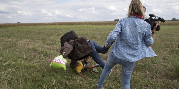Ein Mann, der ein Kind trägt, fällt zu Boden, nachdem ihm eine Kamerafrau ein Bein gestellt hat Ein Mann, der ein Kind trägt, fällt zu Boden, nachdem ihm eine Kamerafrau ein Bein gestellt hat