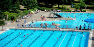 Zwei blaue Schwimmbecken und badende Menschen vor grünem Rasen