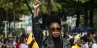 Eine Frau geht mit erhobener Hand am Rande einer Demonstration