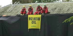 Greenpeace-Aktivisten sitzen in roten Overalls und Helmen auf dem Haus von Rishi Sunak, das mit schwarzen Tüchern zugehängt haben