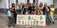 Shezrazad bleibt steh auf einem Schild, dahinter Frauen mit Kindern im Arm