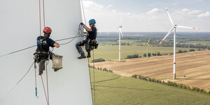 Industriekletterer beim Arbeiten am 55 Meter langen Rotorblatt einer Windkraftanlage, im Hintergrund sind in der Landschaft weitere Windkraftanlagen zu sehen