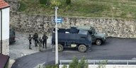 Polizeiwagen und bewaffnete Männer stehen vor einer Feldsteinmauer