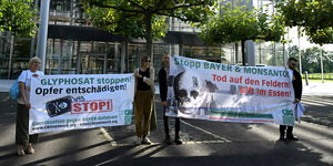 Vier Personen halten vor der Konzernzentrale von Bayer-Konzernzentrale Banner in den Händen; Glyphosat stoppen ! Opfer entschädigen ! Stop !