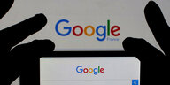 Google-Emblem von zwei schwarz behandschuten Händen gehalten