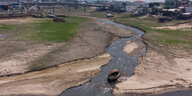 Stark ausgetrocknetes Flussbett mit einem Rest Wasser, im Hintergrund Ausläufer einer Stadt