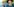 Selfie: weißer Mann mit Hut, Bart und Brille, aufgenommen in einem schmalen Holzkanu, im Hintergrund ist ein Mann zu sehen, der das Ruder eintaucht