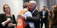 US-Präsident Joe Biden umarmt einen Mann mit orangener Warnweste, auf der hebräische Buchstaben und ein orangenes Kreuz auf weißem Hintergrund zu sehen ist