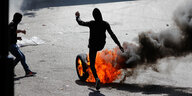 Ein Demonstrant kickt einen brennenden Autoreifen auf eine Straße