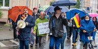 Eine Gruppe von Demonstranten geht mit Regenschirmen eine Straße entlang
