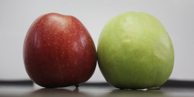 Ein roter und ein grüner Apfel liegen auf einem Tisch. Ein roter und ein grüner Apfel liegen auf einem Tisch.
