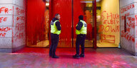 Zwei Polizisten vor dem mit roter Farbe bespritztem Eingang eines Gebäudes