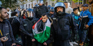 Eine Person mit palestinensischer Fahne wird von Polizisten abgeführt