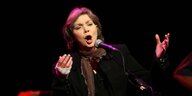 Nanci Griffith singt mit offenem Mund in ein Mikrofon