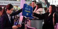 Eine Szene am Check-In-Schalter, eine Frau übergibt eine blaue Tasche.