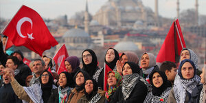 Menschen stehen auf einer Brücke mit türkischen Flaggen vor der Silhouette Istanbuls