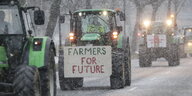 Traktoren fahren bei Schneefall bei einer Demonstration von Bauern über eine Straße. Auf einem Traktor haben Landwirte dabei ein Schild mit der Aufschrift "Farmers For Future" befestigt. Als Reaktion auf die Sparpläne der Bundesregierung hat der Bauernver