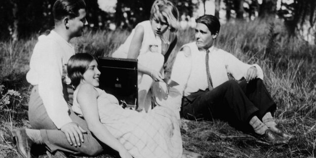 Filmstill aus einem Schwarz-Weiß-Film: Vier junge Menschen sitzen auf einer Wiese, zwischen ihnen steht ein Picknickkorb, hinter ihnen Bäume. Die Szene lässt erahnen, dass sie sich am Wannsee befinden.