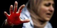 Eine Frau die Handfläche ihrer rechten Hand mit roter Farbe bemalt.