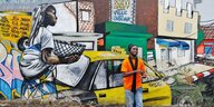 Mann steht vor einem grell bemalten Wandgemälde mit Taxi