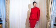 Sahra Wagenknecht trägt ein rotes Kostüm und steht vor der Textiltapete eines Hotelzimmers