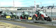 Eine Reihe von Traktoren auf einer Straße vor dem Gelände des Frankfurter Flughafens. Im Hintergrund stehen Passagierflugzeuge