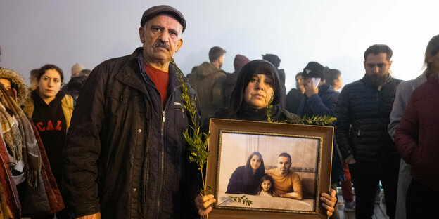 Ein älteres Ehepaar in einer Menschenmenge trägt ein Bild von einer jungen Familie vor sich her. Sie trauern um ihre Familie, die dem Erdbeben zum opfer gefallen sind