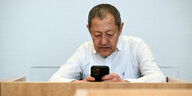 Akif Pirincci sitzt im Gerichtssaal und schaut auf sein Smartphone.