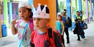 Kleine Schulkinder mit Pappkrone und Rucksäcken gehen über den Schulhof