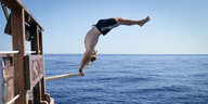 Eine Person macht einen Handstand auf einer Planke über dem offenen Meer.