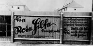 Werbung an einem Bretterzaun für die Rote Hilfe 1924 - in altdeutscher Schrift steht: Die Rote ist die Kampforganisation gegen Faschismus und bürgerliche Klassenjustiz