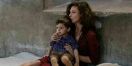 Szene aus einer Fernsehserie: Eine Mutter sitzt mit einem kleinen Kind im Arm auf dem Boden.