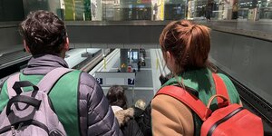 Zwei Helfer:innen der Berlin Arrival Support, Sergej und Viktoria, fahren am Hauptbahnhof die Rolltreppe zum Gleis runter.