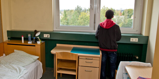 Ein Junge steht im Zimmer seiner Flüchtlingsunterkunft und schaut aus dem Fenster Ein Junge steht im Zimmer seiner Flüchtlingsunterkunft und schaut aus dem Fenster