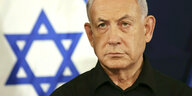 Benjamin Netanjahu steht vor der Flagge Israels und blickt ernst in die Ferne
