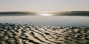 Ein Priel im Wattenmeer zwischen Cuxhaven und der Insel Neuwerk. Im Sand ist ein Muster zu sehen.