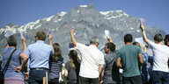 Bewohner von Glarus stehen in kurzen Hosen und Röcken auf einem Holzposest und halten Abstimmungskarten in die Höhe