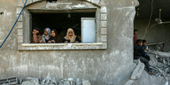 Menschen blicken aus dem Fenster eines zerstörten Wohnhauses