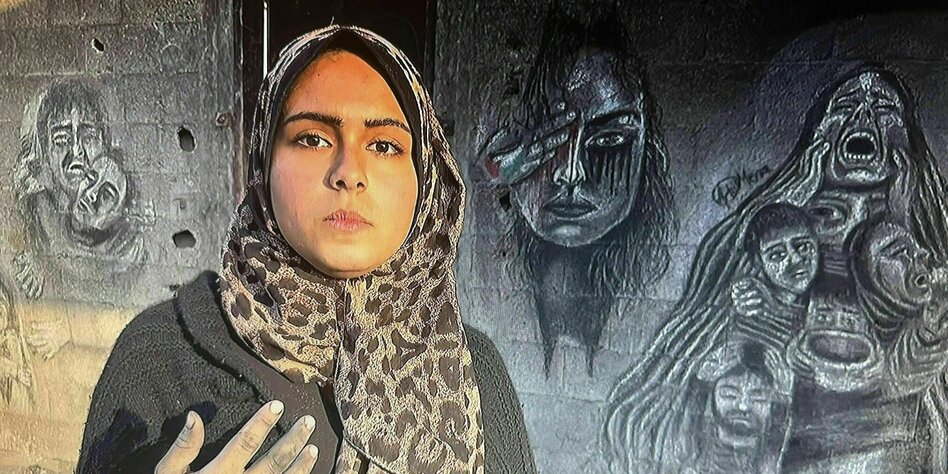 Menna Hamouda steht vor ihren Bildern, die sie an eine Mauer gemalt hat. Das Bild in der Mitte ist ein Selbstporträt, aus ihrem rechten Auge fließen schwarze Tränen , daneben eine schreiende Frau, deren Haare mehereer Menschen umfangen