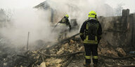 Zwei Feuerwehrmänner in den noch rauchenden Trümmern eines Hauses