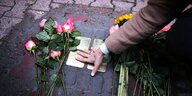 Eine Frau legt Blumen nieder an Stolpersteinen