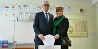 Ein Mann und eine Frau stehen vor einer Wahlurne und werden ihren Stimmzettel einwerfen