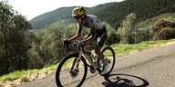 Guillermo Juan Martinez sitzt auf seinem Rennrad und strampelt einen Berg hoch, im Hintergrund bewaldete Hügel