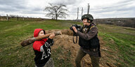 Ein junge hält einen Ast wie mit eine Panzerfaust und wird von einer Journalistin fotografiert.