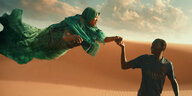 Ein Mann vor einer Düne hält die Hand einer Frau, die fliegt