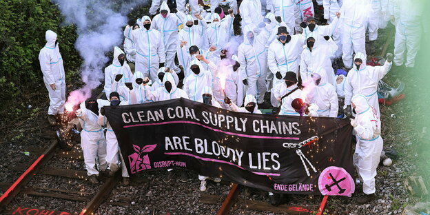 Zahlreiche Menschen in weißen Overalls stehen auf einem Bahngleis. Vor ihnen ein großes Banner mit der Aufschrift "Clean Coal Supply Chains are bloody lies"