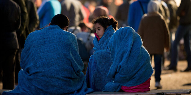 Flüchtlinge sitzen in Decken gewickelt Flüchtlinge sitzen in Decken gewickelt
