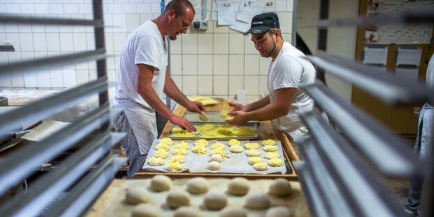 Die Bäcker Mattias Geißler (l) und Patrick Pötsch (r) bereiten Käsebrötchen auf das Backen vor.