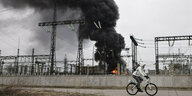 Ein Mann auf dem Fahrrad radelt an einem brennenden Kraftwerk vorbei